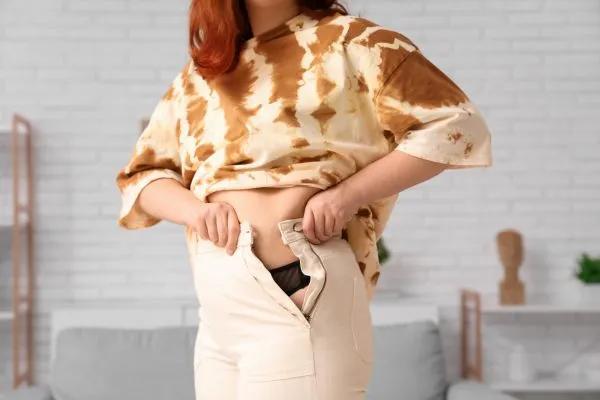 Image of woman trying to do her trousers up after pregnancy weight gain Isle of Isla