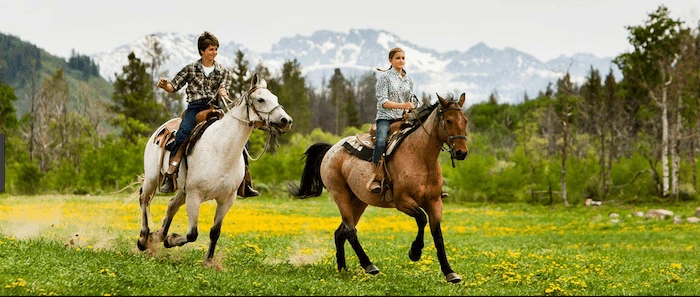Confident plus-size woman riding Isle of Isla a horse through a field with a smile on her face.